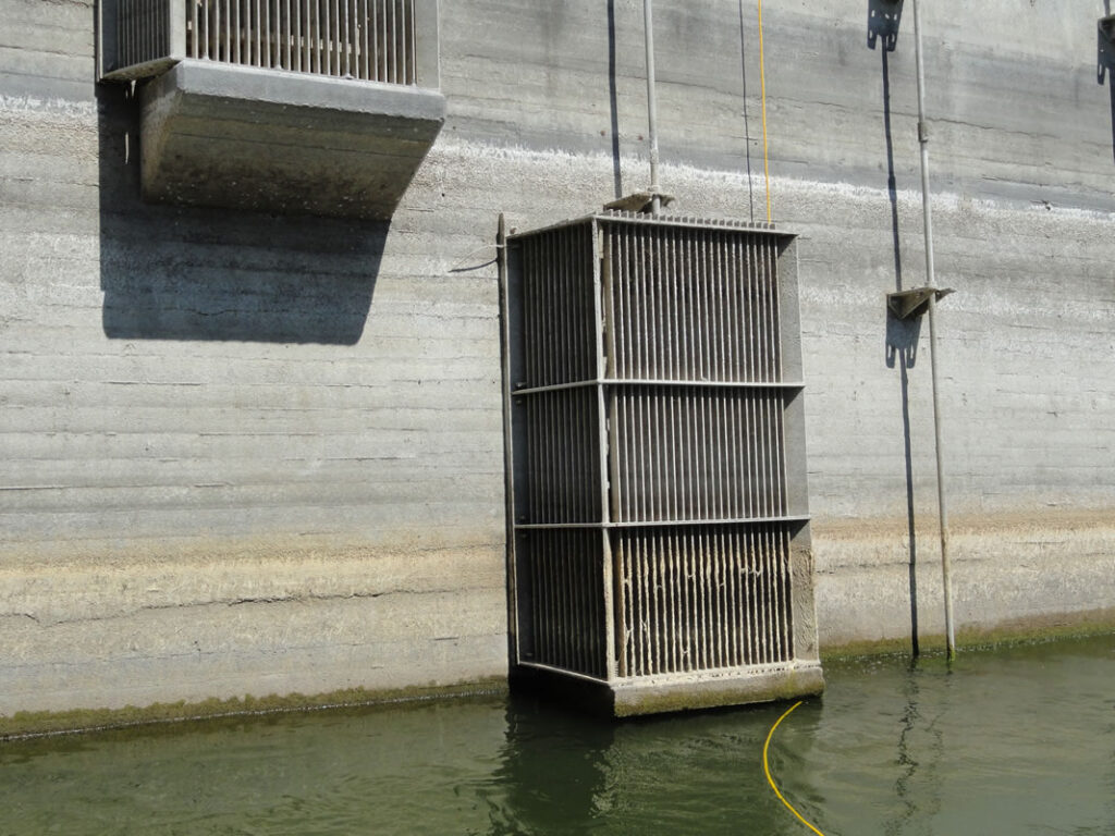 Large metal cage suspended over water near a concrete wall.