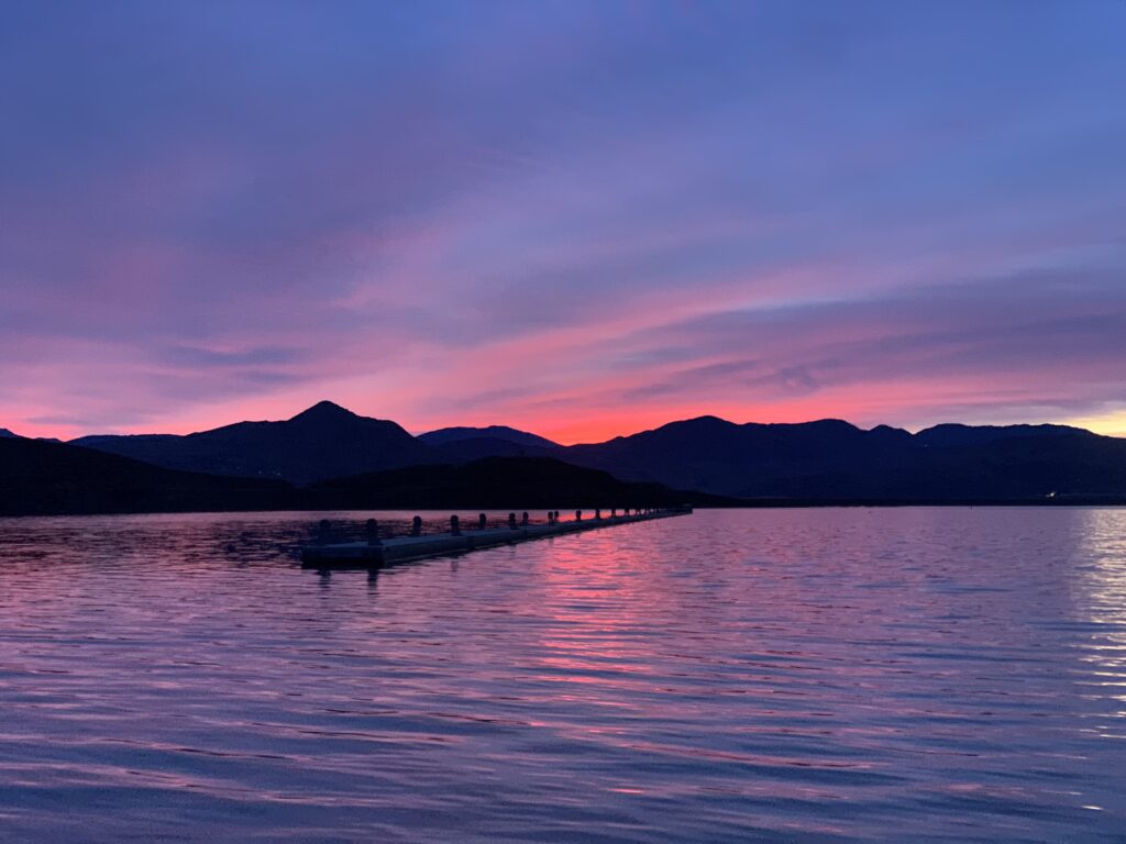 Serene lake at sunset with silhouetted mountains and a pink-purple sky.