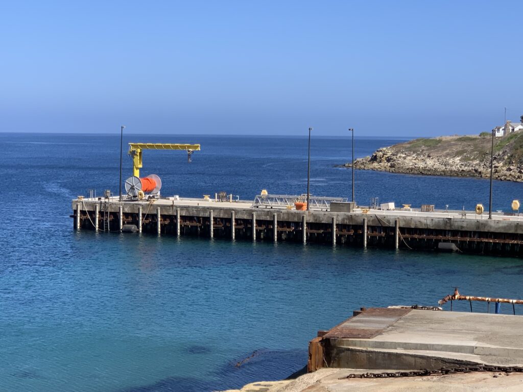 Pier with a crane extending over calm blue sea under clear sky.